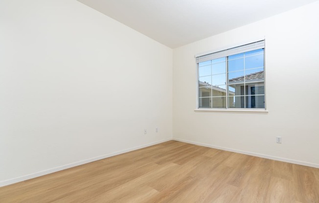 a bedroom with white walls and wood floors and a window