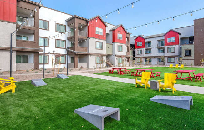 A grassy area with picnic tables and benches in front of apartment buildings.