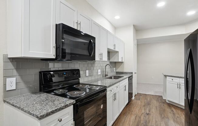 a kitchen with white cabinets and black appliances and a black microwave at La Ventura Apartments, Plano, 75093
