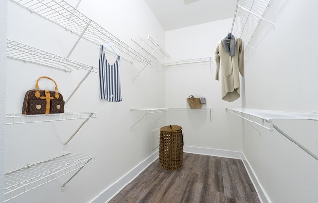 a walk in closet with white walls and shelves and a closet with baskets and bags