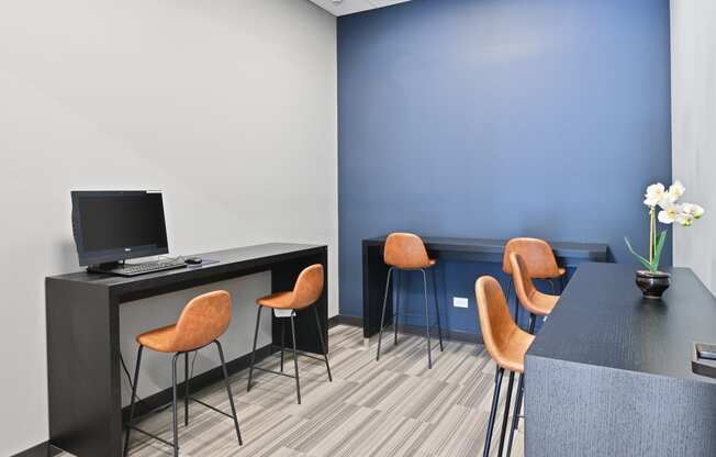 a computer desk and orange chairs in a room with a blue wall