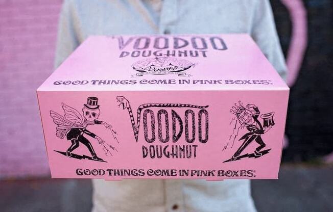 a person holding a pink box that says voodoo doughnut