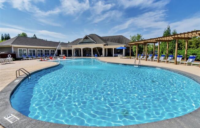 Sparkling pool with fountains, and lounge chairs under a wooden pergola near a clubhouse