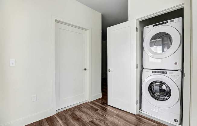 A white door is open to a cabinet with two washing machines in it.