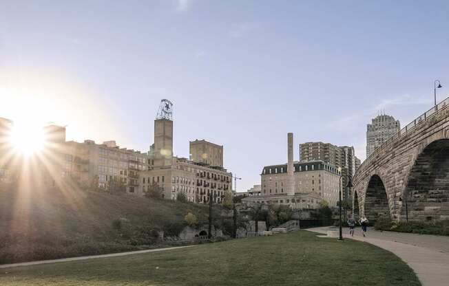 A sunny day in a city with a grassy area in the foreground and buildings in the background.