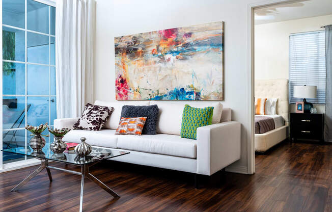 Living Room with Wood-Style Flooring, White Couch, Glass-Top Coffee Table, Wall Art, and Large Window at Barrington Place, Rancho Cucamonga, CA