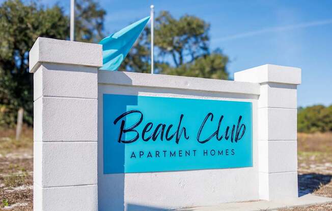 A sign for Beach Club Apartment Homes stands in front of a blue sky.
