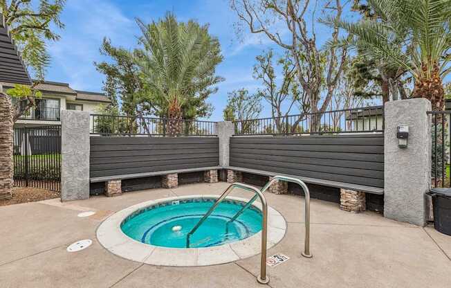 A small pool surrounded by a concrete patio and a metal fence.