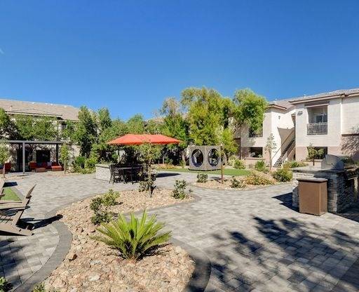 A sunny day at a courtyard with a red umbrella and a circular bench.
