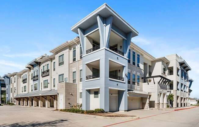 A large, modern apartment complex with multiple balconies and a clear blue sky above.