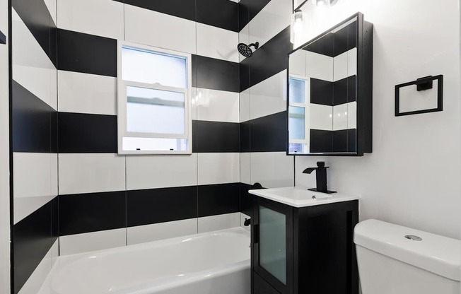 A black and white bathroom with a tub, sink, and mirror at Brookmore Pasadena, CA.