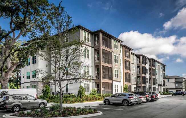 A row of apartment buildings with cars parked in front.