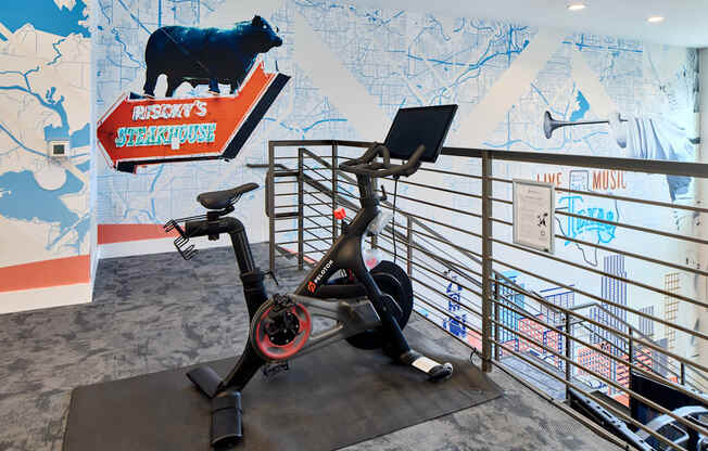 A stationary exercise bike is in front of a wall with a cow on it.