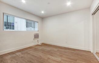 a living room with white walls and wood flooring and a window