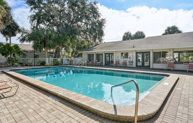 A swimming pool surrounded by a brick patio and a building in the background.