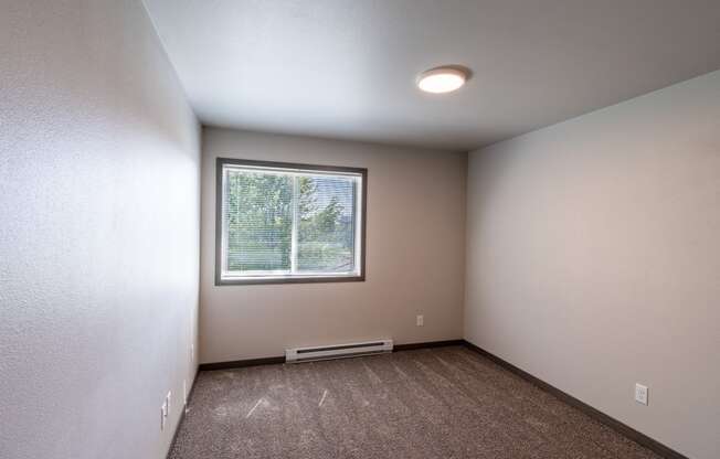 A bedroom with a window and baseboard heater. Fargo, ND Granger Court Apartments.