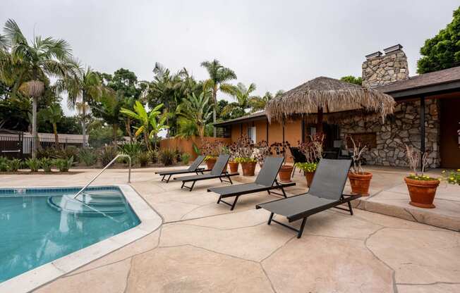 a pool and lounge chairs in front of a house with a thatched roof