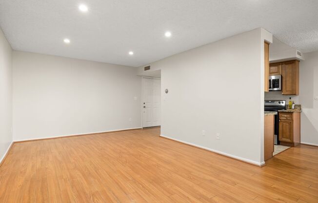 an empty living room with wood flooring and a kitchen