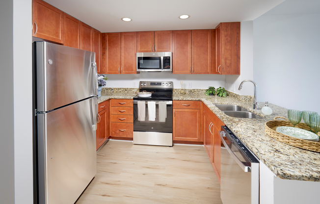 Newly Renovated Ellington Floor Plan Kitchen at Meridian at Grosvenor Station featuring sleek stainless steel appliances, modern vinyl plank wood-style flooring, and updated lighting fixtures that complement existing granite countertops and custom cabinetry.