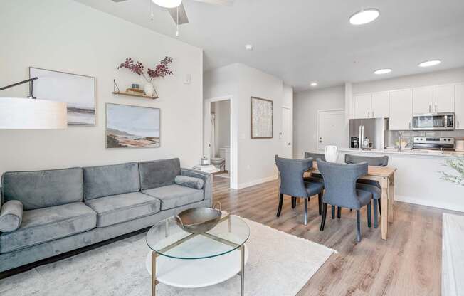 a living room with a couch a table and chairs and a kitchen in the background