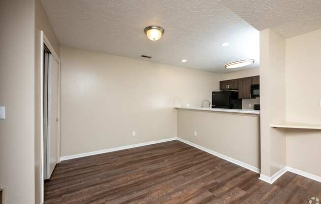 an empty living room with wood flooring and a kitchen