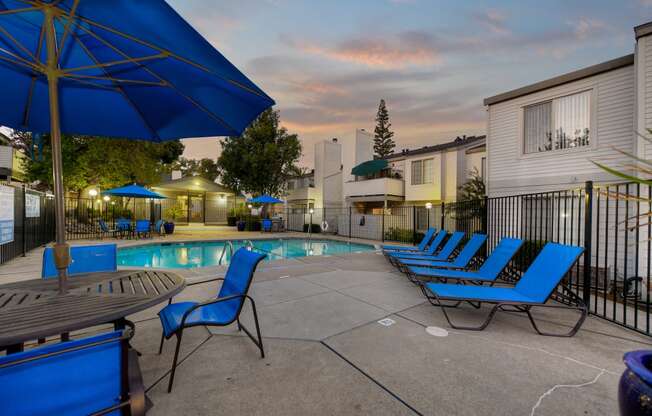 Swimming Pool Lounge Area at dusk with bright blue chairs and umbrellas at Cobblestone Creek Apartments, Roseville