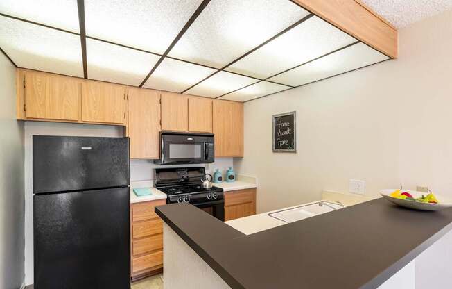 A black refrigerator is in a kitchen with wooden cabinets.