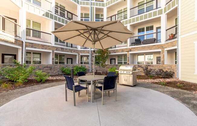 A patio with a table and chairs and an umbrella in front of apartment buildings.