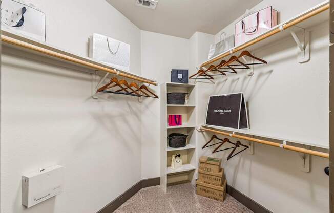 A walk in closet with clothes and a laptop on a shelf.