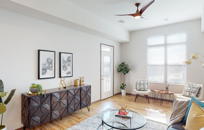 A bright living room here at Van Buren East with wood-style flooring and modern decor. A large window fills the space with natural light, while a cozy seating area creates a warm, inviting atmosphere.
