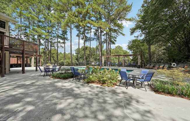 A patio with chairs and a table surrounded by trees.