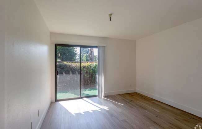 an empty living room with a sliding glass door to a backyard