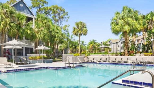 a large swimming pool with chaise lounge chairs and palm trees in front of a building