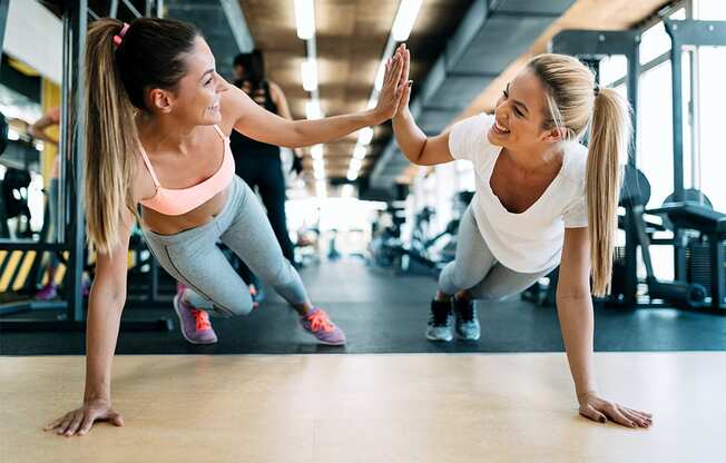 two women giving each other a high five while doing push ups in the gym