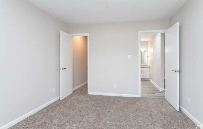 a bedroom with white walls and carpet and a hallway to a bathroom