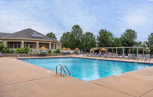 A large outdoor swimming pool with a sun lounger chairs and a building with solar panels on the roof.
