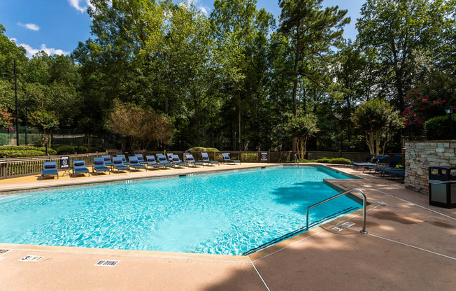 a swimming pool with lounge chairs and trees in the background