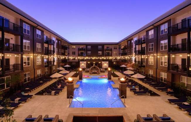 A swimming pool surrounded by lounge chairs and balconies with lights strung up.