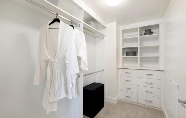 a walk in closet with white robes and a black dresser