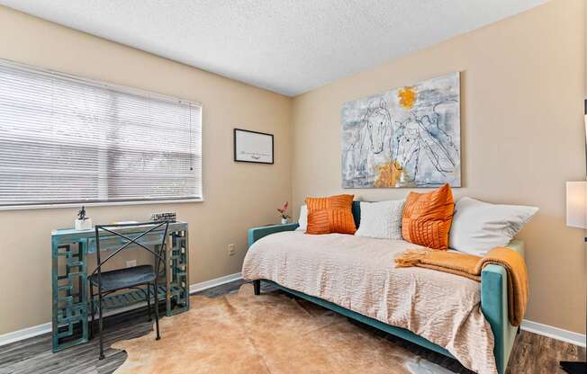 A bedroom with a bed, a desk, and a painting on the wall.