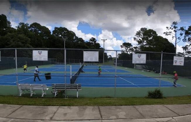 A tennis court with people playing tennis and a cloudy sky.