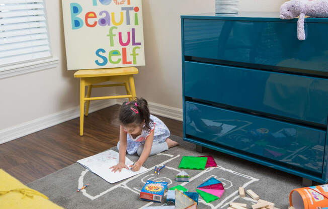 Toddler aged girl sitting on the bedroom floor coloring in a coloring book.