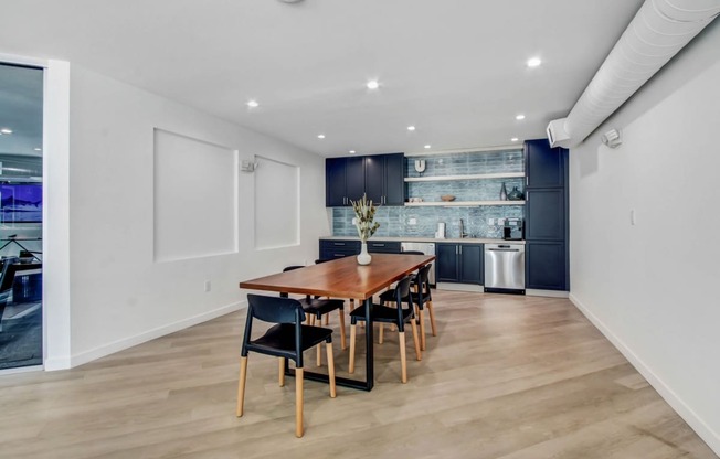 a dining area with a wooden table and chairs and a kitchen in the background