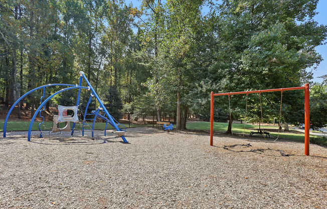 A playground with a blue swing set and a red swing set.