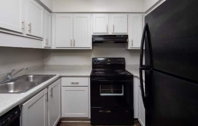 A black refrigerator stands next to a black stove in a kitchen with white cabinets.