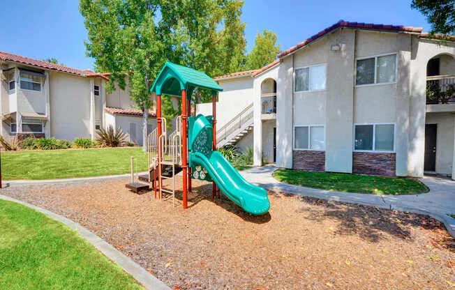 A playground with a green slide in front of apartment buildings.