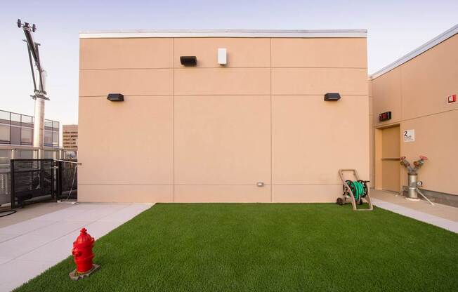 A red fire hydrant is placed on a green lawn in front of a tan building.