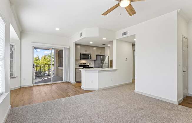 an empty living room with a kitchen and a ceiling fan