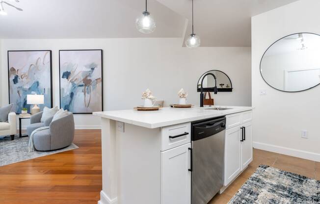 a white kitchen with an island and a living room with a couch and a mirror