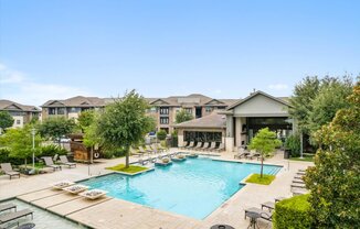 a swimming pool with chaise lounge chairs and trees in front of a building